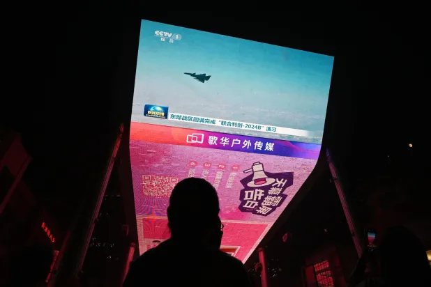 مواطن صيني يتابع عبر شاشة تلفزيون طائرات صينية خلال مناوراتها حول تايوان أمس (أ.ف.ب)