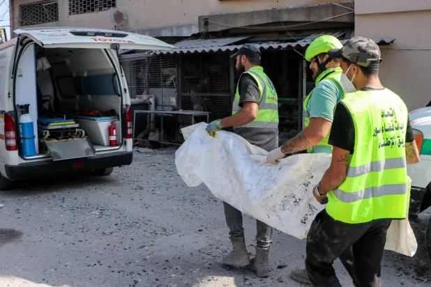 Kana'da İsrail saldırısı sonucu ölen bir sivilin cesedini taşıyan sivil savunma ekibi üyeleri (AFP)