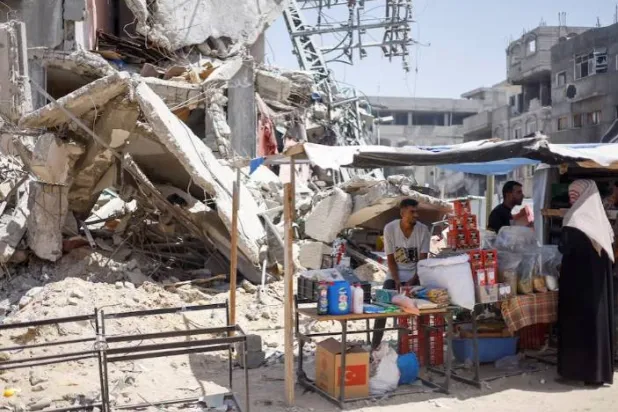 فلسطينيون يتسوّقون في سوق مؤقتة أُقيمت بجوار المباني المدمّرة بغارة جوية إسرائيلية في خان يونس (رويترز)