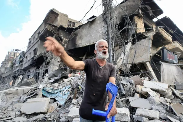 İsrail'in Nebatiye'ye düzenlediği hava saldırılarının yol açtığı büyük yıkımın önünde koltuk değnekleriyle duran Lübnanlı bir adam (AFP)