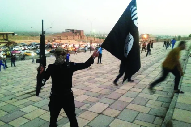 مقاتل من «داعش» يحمل سلاحاً مع علم التنظيم في أحد شوارع مدينة الموصل يوم 23 يونيو 2014 (رويترز)