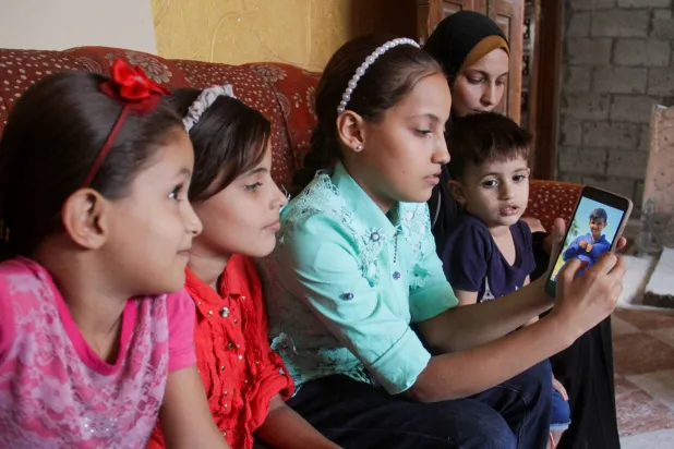 أطفال انفصلوا عن شقيقهم بعد فراره من شمال غزة ينظرون إلى صورته على هاتف جوال (رويترز)