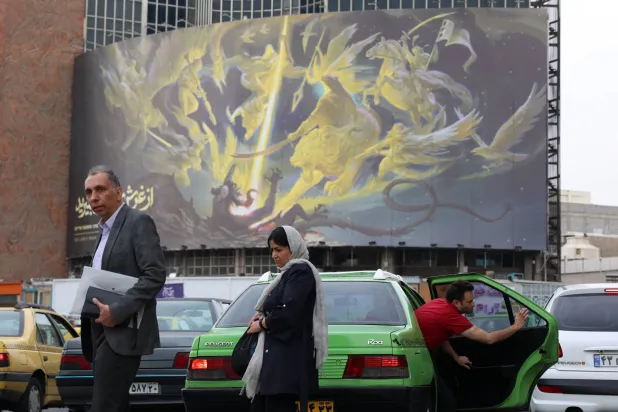 إيرانيون يمرون بجانب لافتة مناهضة لإسرائيل في ساحة ولي عصر وسط طهران اليوم (إ.ب.أ) 