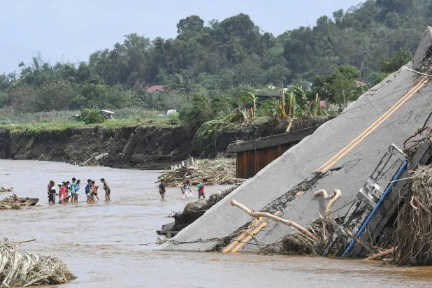أشخاص يعبرون نهراً بجوار جسر بعد أن فاض النهر بسبب الأمطار الغزيرة الناجمة عن العاصفة الاستوائية «ترامي» في لوريل بمقاطعة باتانغاس جنوب مانيلا 25 أكتوبر 2024 (أ.ف.ب)