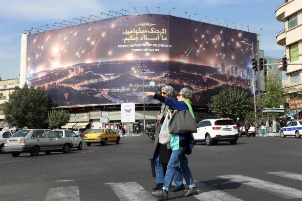 إيرانيات يمشين بالقرب من لافتة معادية لإسرائيل مع عبارة باللغة الفارسية تقول: «إذا كنتم تريدون الحرب فنحن أسياد الحرب» في ساحة انقلاب (الثورة) في طهران (إ.ب.أ)