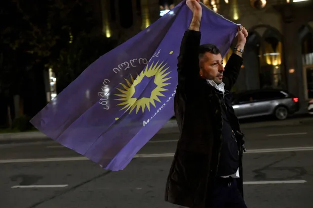 أحد داعمي حزب «الحلم الجورجي» يحمل علم الحزب في الشارع عقب الإعلان عن نتيجة الانتخابات البرلمانية في جورجيا (رويترز)