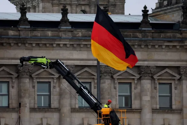 علم ألماني يرفرف أمام مبنى «الرايخستاغ» بينما يعمل رجل على رافعة في برلين (رويترز)