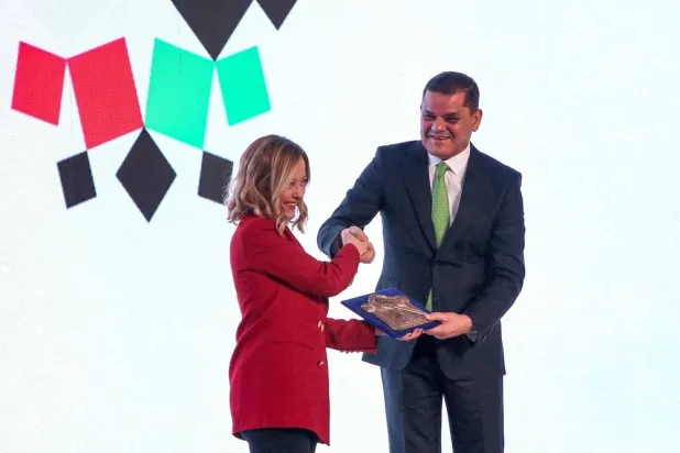Head of Libya's Tripoli-based Government of National Unity (GNU) Abdulhamid al-Dbeibah and Italy's visiting Prime Minister Giorgia Meloni shake hands as they exchange a commemorative plaque during the inauguration of the 30th session of the Libyan-Italian Business Forum at the Tripoli Exhibition Center in Tripoli on October 29, 2024. (AFP) 