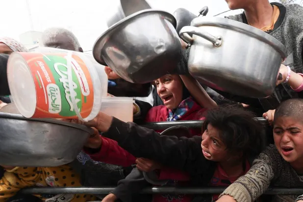 أطفال فلسطينيون يتلقون طعاماً مطبوخاً بواسطة مطبخ خيري وسط نقص الغذاء في رفح (رويترز)