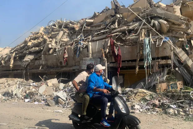 لبنانيان يستقلان دراجة نارية يمران بمبان دمرها القصف الإسرائيلي في حارة حريك بضاحية بيروت الجنوبية أمس (أ.ف.ب)