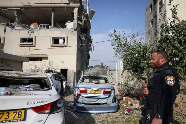 ضابط شرطة إسرائيلي أمام مبنى سكني في مدينة الطيرة العربية وسط إسرائيل تعرّض لأضرار بسبب شظايا اعتراضات الصواريخ التي أُطلقت من لبنان السبت (إ.ب.أ)