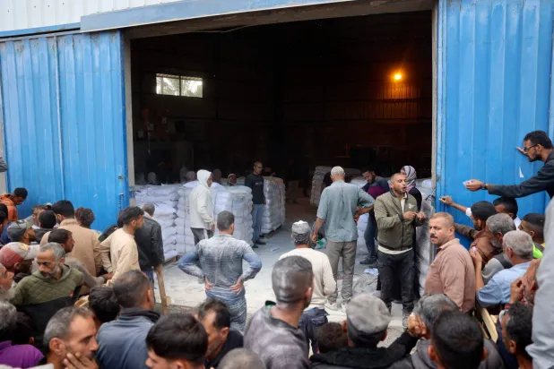 متطوعون يوزعون أكياس الدقيق في مركز توزيع مساعدات وكالة الأمم المتحدة لإغاثة وتشغيل اللاجئين الفلسطينيين (الأونروا) في دير البلح اليوم (أ.ف.ب)