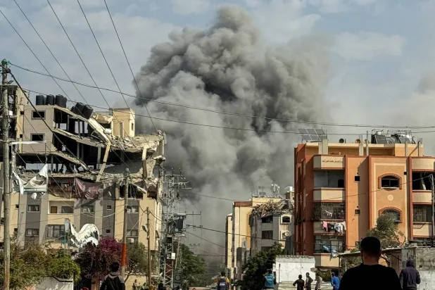 فلسطينيون يشاهدون الدخان يتصاعد بعد الضربات الإسرائيلية في النصيرات بوسط قطاع غزة (رويترز)
