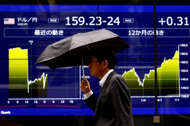 رجل يمشي أمام شاشة إلكترونية تعرض سعر صرف الين الياباني الحالي مقابل الدولار والرسم البياني الذي يوضح حركته في طوكيو (رويترز)