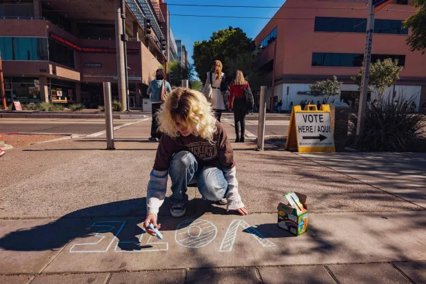 أثينا الناشطة المتطوعة تكتب كلمة «تصويت» على الرصيف قرب مكتب اقتراع في فينيكس بولاية أريزونا في 4 نوفمبر 2024 (أ.ف.ب)