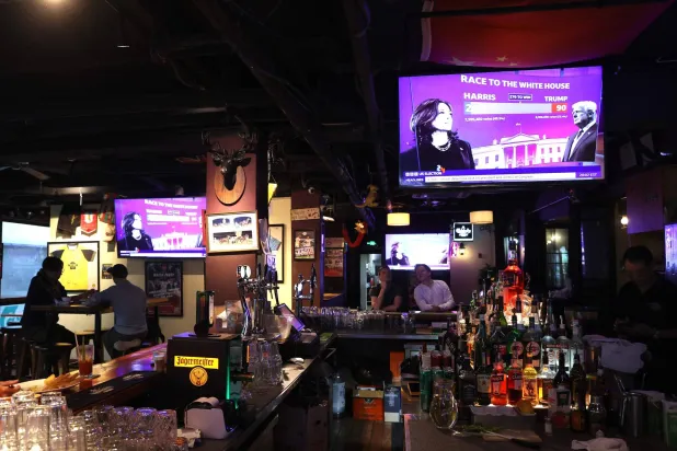 الناس يشاهدون التغطية التلفزيونية للانتخابات الرئاسية الأميركية بإحدى الحانات في شنغهاي (أ.ف.ب)