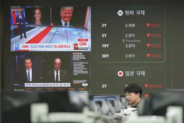 متداول عملات أمام شاشات تعرض صور المرشحَين ترمب وهاريس بغرفة تداول العملات الأجنبية في سيول (أ.ب)