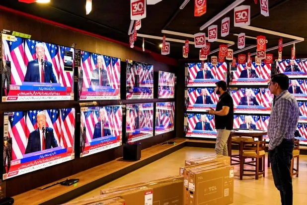 يشاهد رجال بثاً تلفزيونياً بمتجر في إسلام آباد يظهر فيه دونالد ترمب وهو يخاطب مؤيديه في فلوريدا (أ.ف.ب)