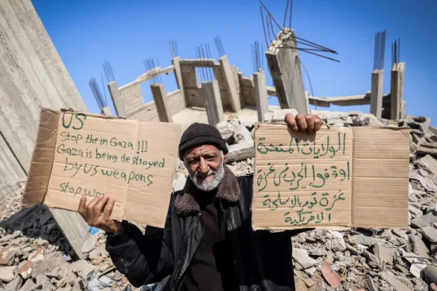 Bureyc Mülteci Kampı’nda, üzerinde Trump'tan Gazze'ye yönelik savaşı durdurmasını isteyen mesajın yer aldığı pankartlar tutan bir Filistinli (AFP)