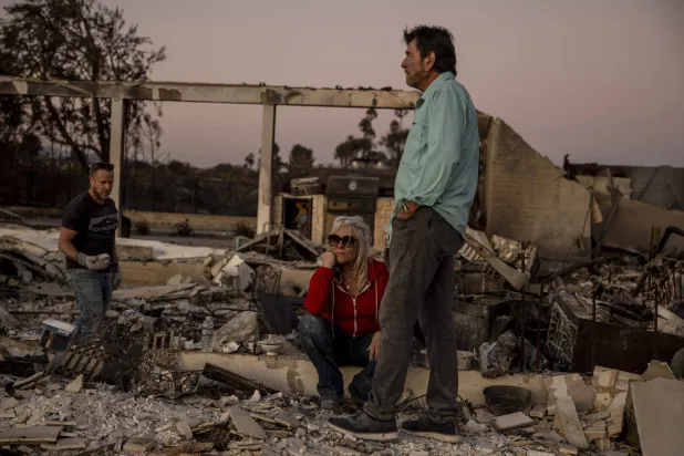 امرأة وزوجها وسط أنقاض منزلهما الذي أتى عليه الحريق في كاماريللو (أ.ب)