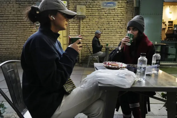 امرأتان تشربان الشاي في الهواء الطلق بمقهى شمال طهران (أ.ب)