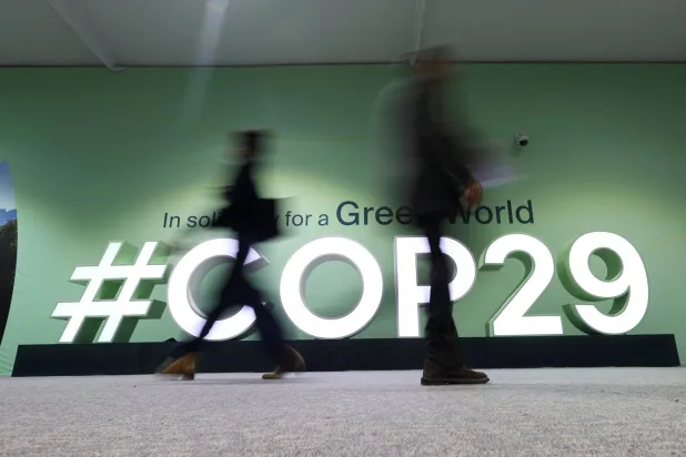 شخصان يمران أمام شعار «كوب 29» خلال مؤتمر الأمم المتحدة لتغير المناخ في باكو (رويترز)