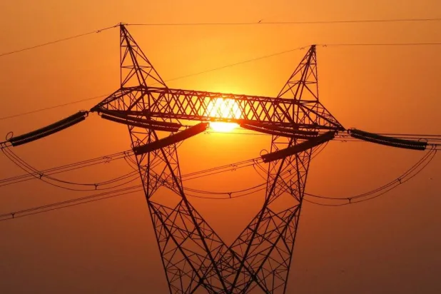The sun sets behind high-voltage power line poles (Reuters)
