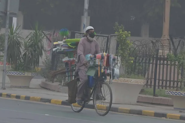 رجل يركب دراجة على طريق وسط الضباب الدخاني في لاهور (إ.ب.أ)