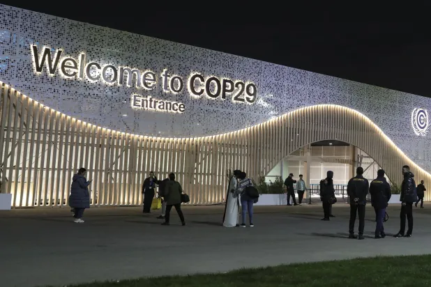 يقف المشاركون وموظفو الأمن خارج مكان انعقاد مؤتمر الأمم المتحدة لتغير المناخ في باكو (إ.ب.أ)