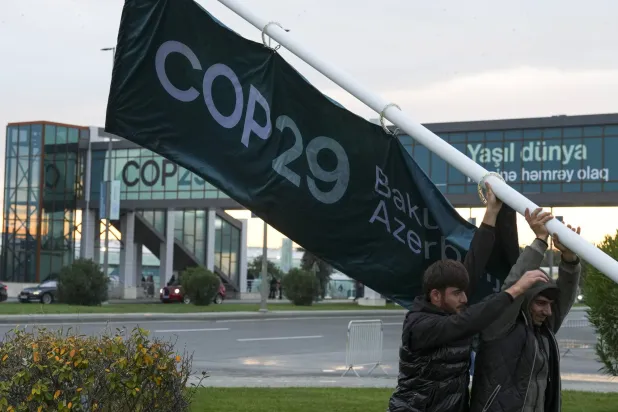 أشخاص يقومون بتعديل لافتة خارج مكان انعقاد قمة المناخ التابعة للأمم المتحدة (أ.ب)