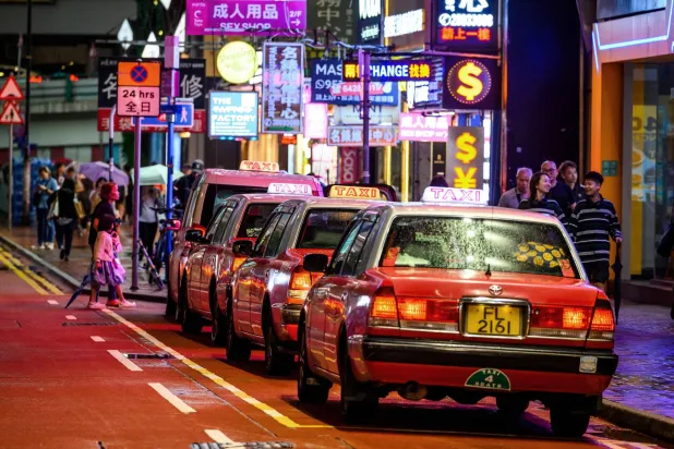 سيارات أجرة في أحد الشوارع التجارية والخدمية بجزيرة هونغ كونغ ليلاً (أ.ف.ب)