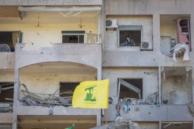 علم «حزب الله» يظهر أمام مبنى دمره القصف الإسرائيلي في بيروت (رويترز)