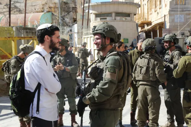 ناشط من المستوطنين اليهود بحماية جنود إسرائيليين خلال احتفالات عيد المظال اليهودي في منطقة البلدة القديمة بالخليل (د.ب.أ)