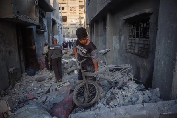 صبي فلسطيني ينقذ دراجة هوائية تالفة من بين أنقاض منزل دُمر في غارة إسرائيلية على مخيم البريج للاجئين في وسط قطاع غزة الأحد (الفرنسية)