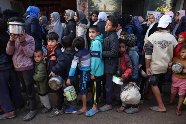 نازحون فلسطينيون ينتظرون في طوابير للحصول على الغذاء في مركز توزيع في دير البلح وسط قطاع غزة (أ.ف.ب)