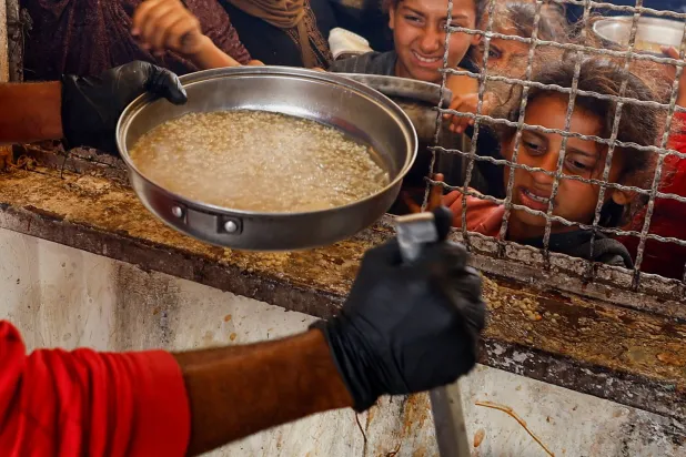 فتاة تتفاعل مع تجمع الفلسطينيين لتلقي الطعام الذي تعده جمعية خيرية وسط أزمة الجوع (رويترز)