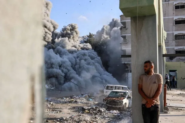 A man hides behind a column as smoke and dust spread as a result of an explosion during an Israeli raid targeting a school in the Al-Zaytoun neighborhood on the outskirts of Gaza City on September 1, 2024 (AFP)