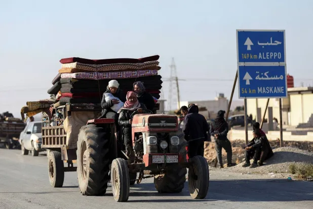 نازحون فروا من ريف حلب يركبون سيارة تحمل أمتعتهم بجوار إشارة طريق في حلب (رويترز)