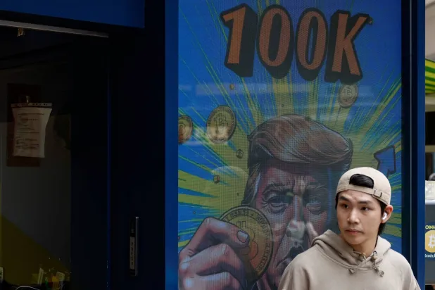 تظهر صورة لترمب وهو يحمل عملة «بتكوين» خارج متجر لتداول العملات المشفرة بعد ارتفاع سعرها إلى أكثر من 100 ألف دولار في هونغ كونغ (رويترز)