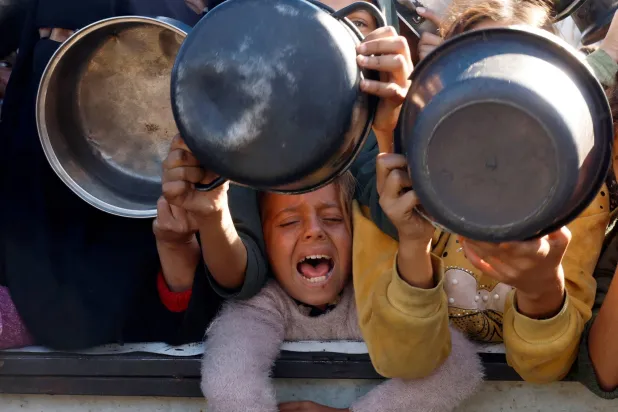 أطفال فلسطينيون ينتظرون تلقي الطعام الذي يطبخه أحد المطابخ الخيرية وسط أزمة الجوع مع استمرار الحرب في غزة (رويترز)
