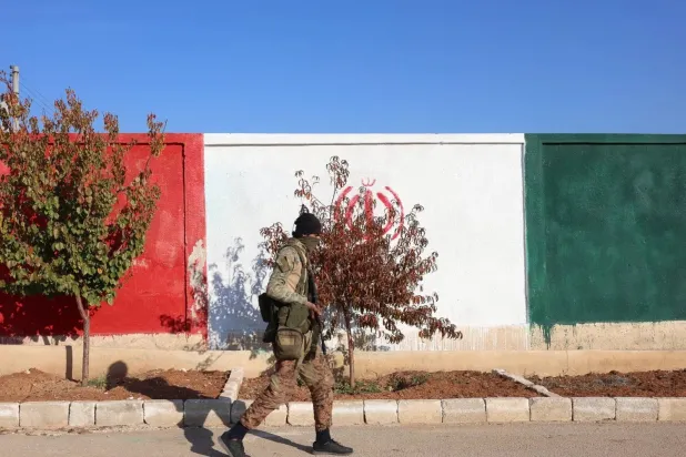 An opposition fighter crosses a wall painted with the colors of the Iranian flag in the town of Khan Sheikhoun, in rural Idlib, at a military site belonging to Iranian forces, after Syrian opposition forces took control of the town (EPA).