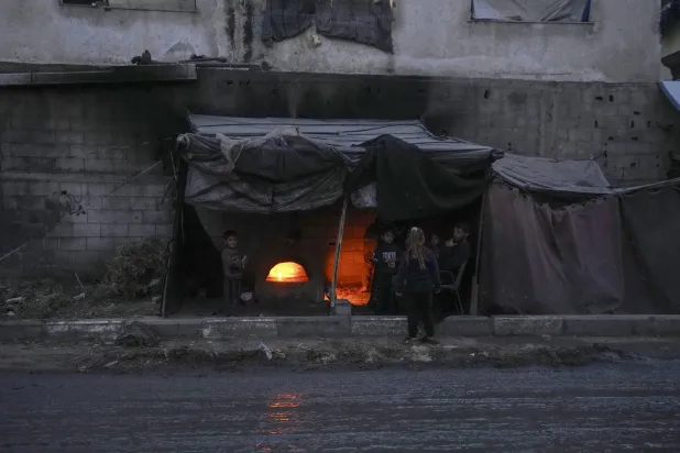 Displaced Palestinians sit next to a makeshift oven in a tent set up on an area in Deir al-Balah, Gaza Strip Thursday, Dec. 5, 2024. (AP Photo/Abdel Kareem Hana)