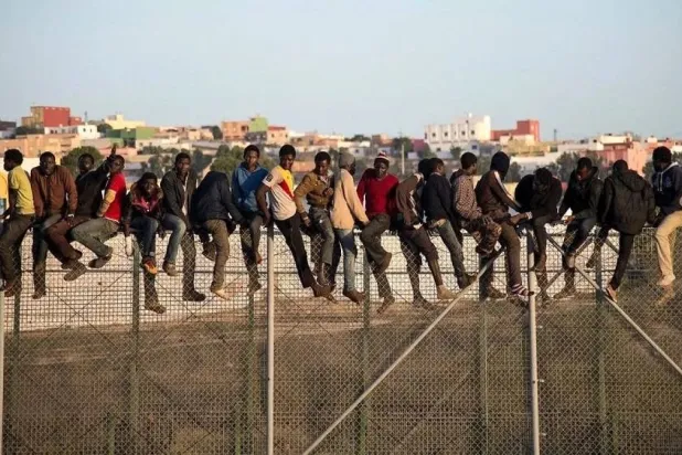 A file photo of would-be immigrants stand atop a border fence separating Morocco from the enclave of Melilla. (AFP)