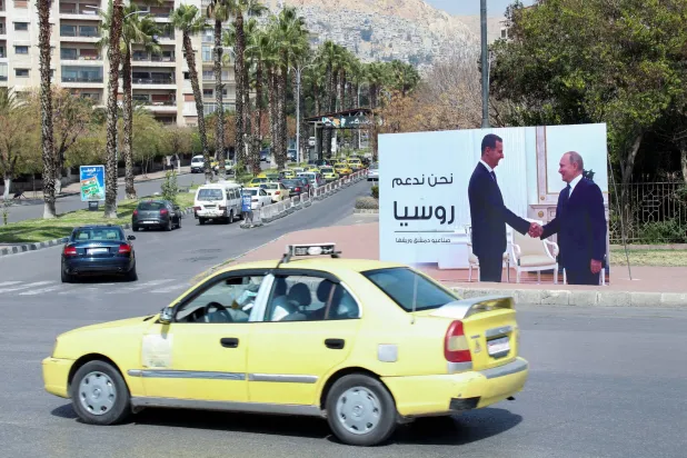 FILE PHOTO: Cars drive past a poster depicting Syrian President Bashar al-Assad shaking hands with Russian President Vladimir Putin in Damascus, Syria, March 7, 2022. REUTERS/Firas Makdesi/File Photo