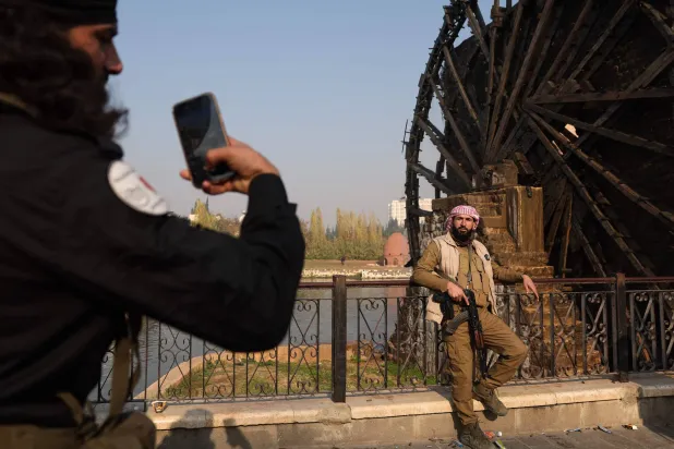 A Syrian anti government fighter poses for a picture in front of one of the water wheels, or norias, of Hama, after forces captured of the city of Hama on December 6, 2024. (Photo by OMAR HAJ KADOUR / AFP)
