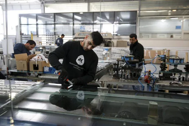 عمال فلسطينيون يعملون في مصنع للبناء بالألمنيوم بمستوطنة معاليه أدوميم اليهودية بالضفة الغربية (رويترز)