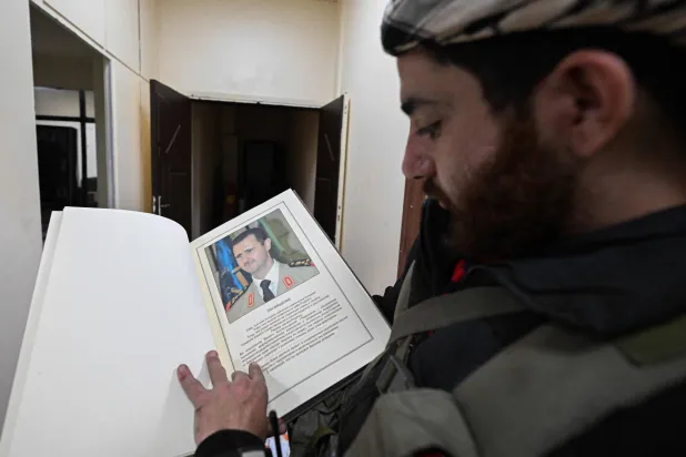 عنصر من القوات العسكرية يتفحص وثيقة باللغة الروسية تحمل صورة الرئيس المخلوع بشار الأسد داخل مقر الأمن العسكري التابع لوزارة الدفاع في منطقة كفر سوسة بدمشق (أ.ف.ب)