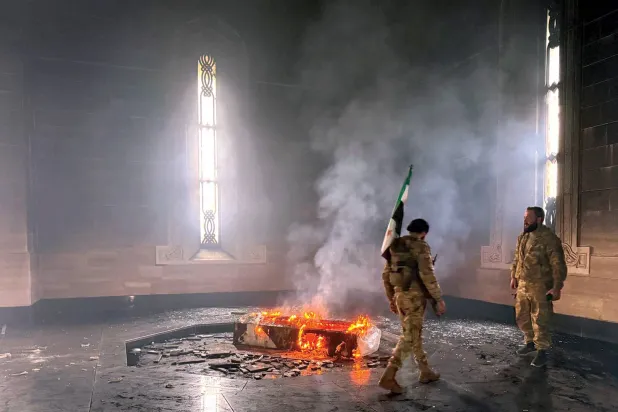  مسلحان يقفان أمام ضريح حافظ الأسد بعد إضرام النار به في قرية القرداحة بمحافظة اللاذقية أمس (أ.ف.ب)

 