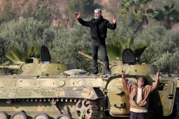 رجلان سوريان يُظهران تخلي القوات السورية عن مركباتها العسكرية قرب مطار المزة العسكري خارج دمشق (أ.ف.ب)