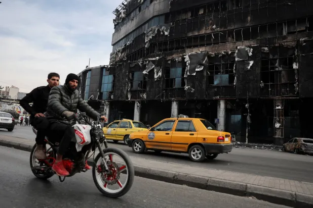 سوريان يركبان دراجة نارية بالقرب من مبنى محترق لإدارة الهجرة والجوازات في دمشق (رويترز)